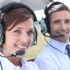 Uśmiechnięta kobieta i mężczyzna w słuchawkach lotniczych. Czy pilot może mieć wadę wzroku? Tak, jeśli jest ona skorygowana.
