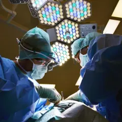 Chirurdzy w maseczkach i czepkach podczas operacji pod jasnym światłem lampy chirurgicznej.