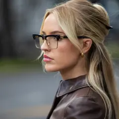 Eleganckie oprawki, które odmładzają, podkreślają urodę blondynki w brązowej kurtce.