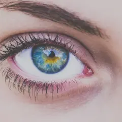 Zbliżenie na tęczówkę oka w odcieniach niebieskiego i żółtego, otoczoną rzęsami.