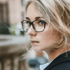 Kobieta w okularach z antyrefleksem, z blond włosami spiętymi w kok, patrzy w bok.