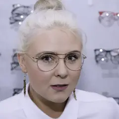 Blondynka z okularami w złotych oprawkach, wybiera nowe okulary w salonie optycznym.