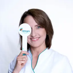 Uśmiechnięta kobieta w białym fartuchu zasłania jedno oko tabliczką z logo "Optegra Eye Health Care". To symbol nagłej poprawy wzroku.