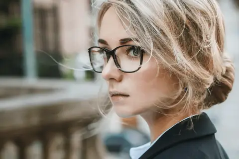 Kobieta w okularach z antyrefleksem, z blond włosami spiętymi w kok, patrzy w bok.
