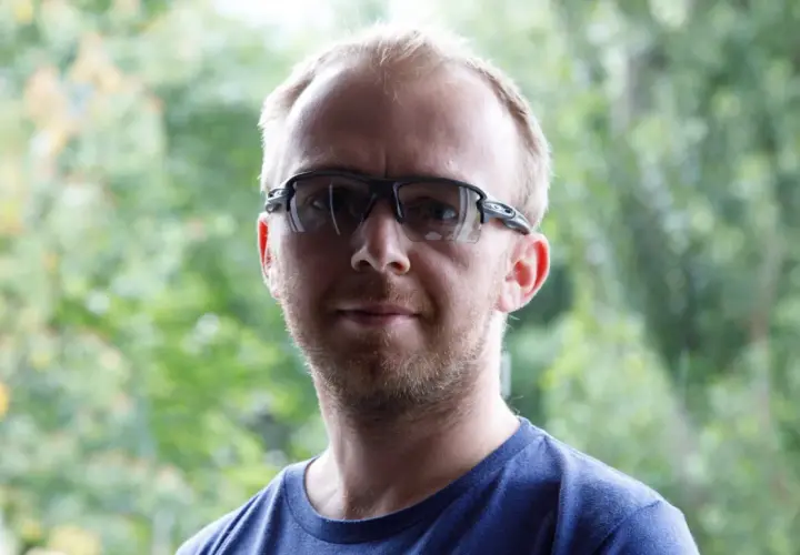 Mężczyzna w okularach sportowych na tle zieleni.