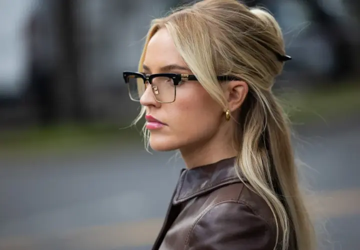 Eleganckie oprawki, które odmładzają, podkreślają urodę blondynki w brązowej kurtce.