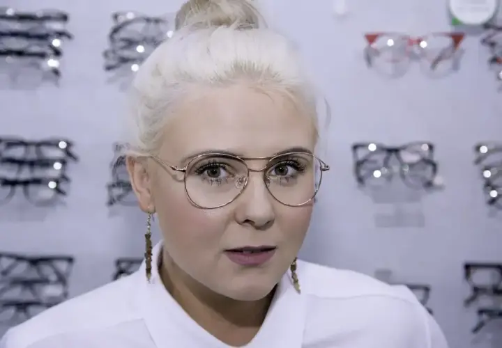 Blondynka z okularami w złotych oprawkach, wybiera nowe okulary w salonie optycznym.