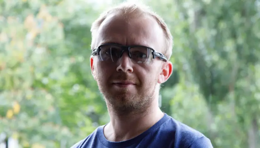 Mężczyzna w okularach sportowych na tle zieleni.