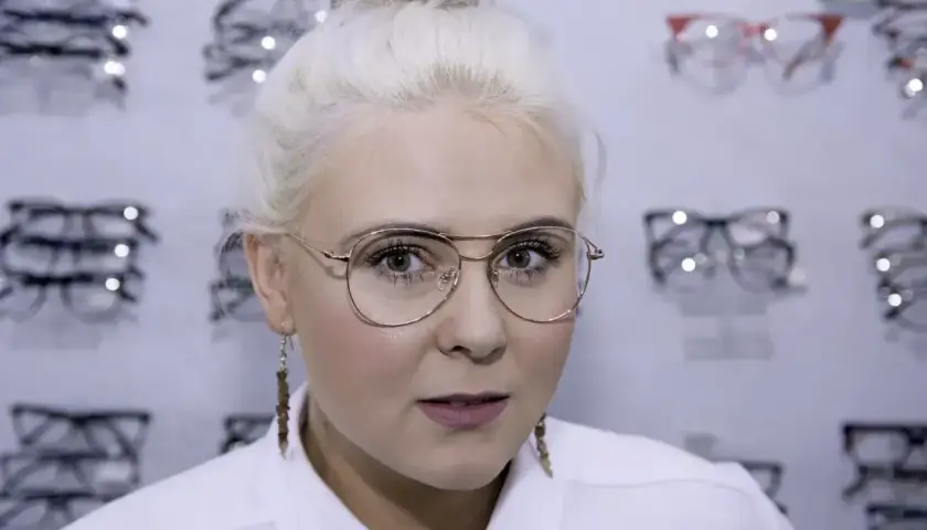 Blondynka z okularami w złotych oprawkach, wybiera nowe okulary w salonie optycznym.
