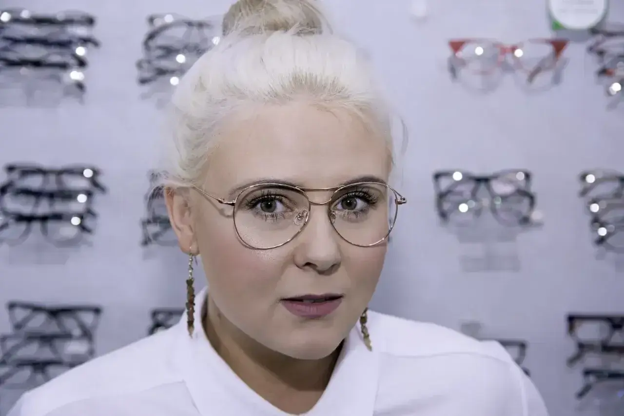 Blondynka z okularami w złotych oprawkach, wybiera nowe okulary w salonie optycznym.